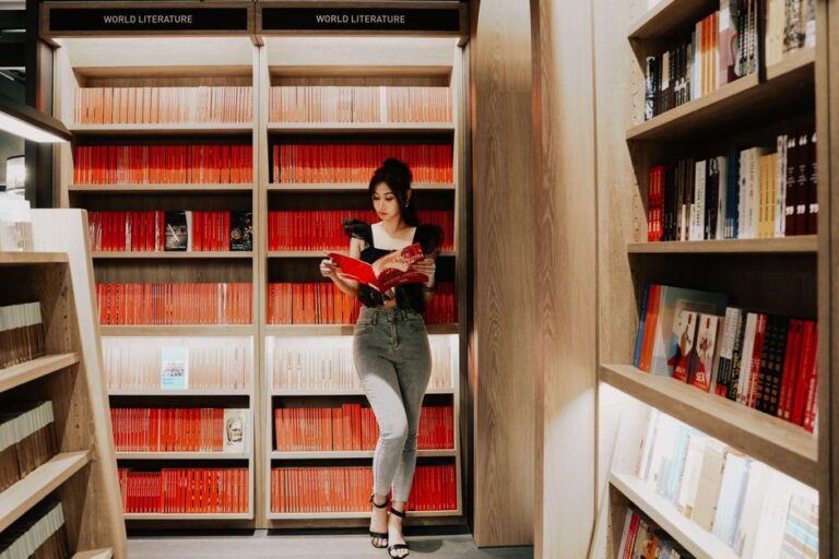 A woman stands reading a book in a contemporary library setting.