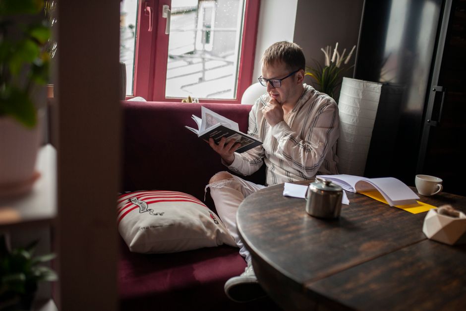 Intelligent content female reading volume of fascinating book near window of lounge in daytime
