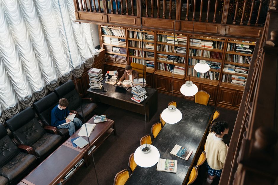A woman stands reading a book in a contemporary library setting.