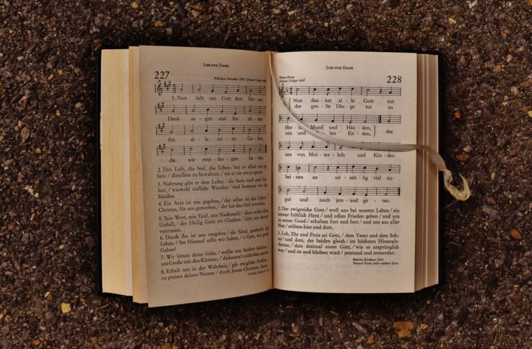 An open hymn book with musical notes laying on earthy ground, featuring sheet music and lyrics.