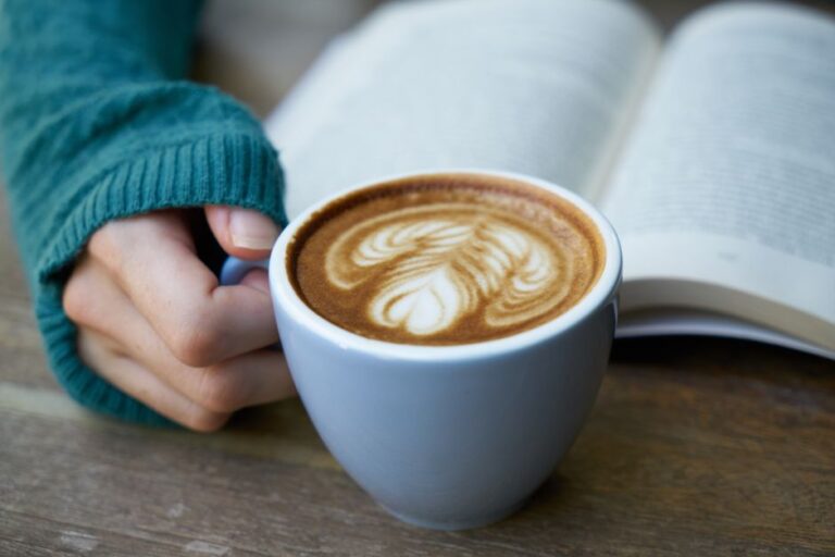A warm cup of latte with beautiful latte art, next to an open book on a rustic table.